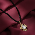 Black beaded necklace with a gold pendant and a large clear crystal on a maroon fabric background