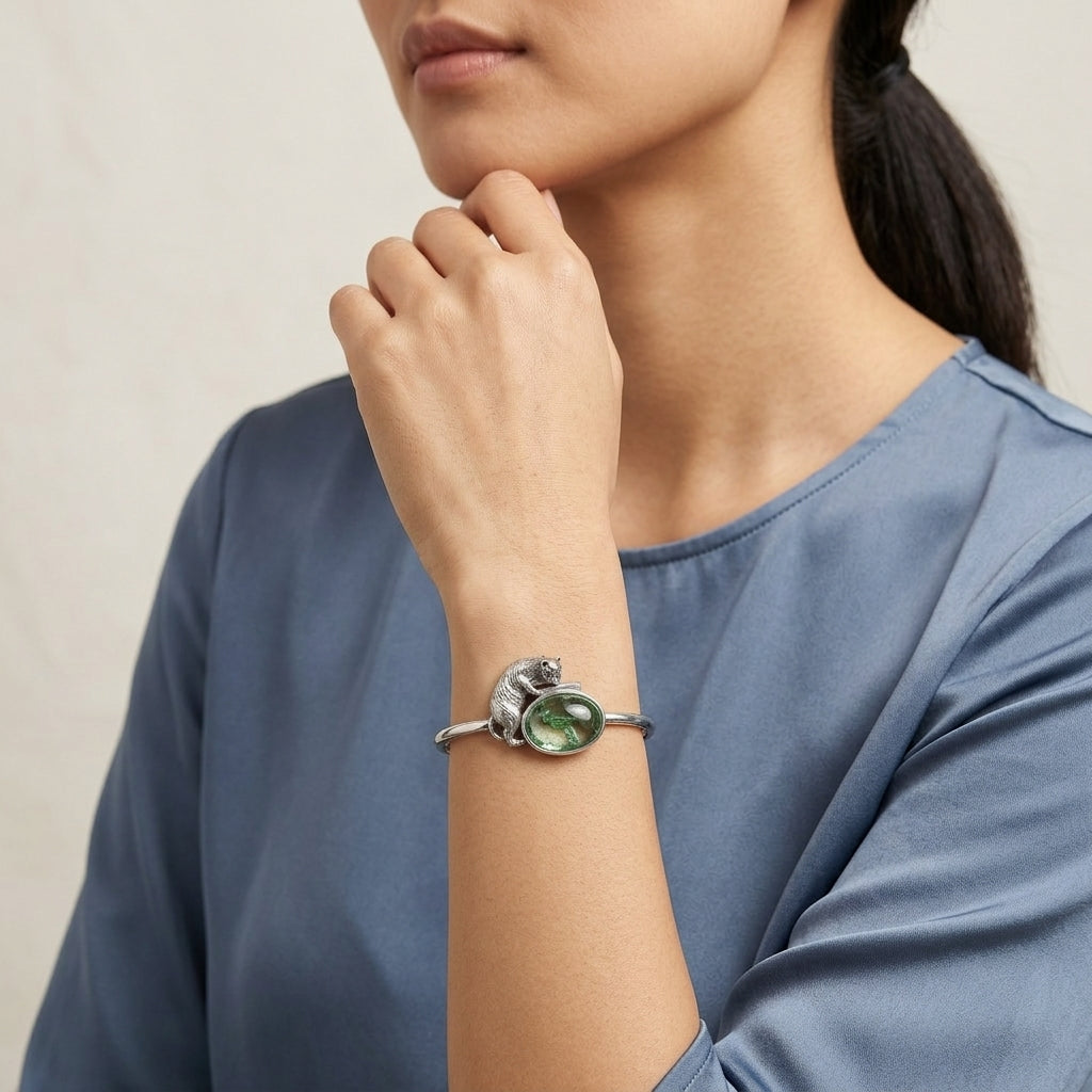 Woman wearing a silver cat and fish bowl design bracelet with a green stone on a neutral background