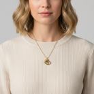 Woman wearing a gold necklace with a pendant against a neutral background