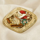 Gold brooch with a festive design of a teddy bear on a sled in a Santa hat on a beige fabric background