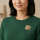 Woman wearing a green sweater with a decorative teddy bear and sled brooch on a neutral background