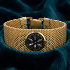 Gold bracelet with a central black stone design on a dark blue fabric background