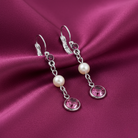 Silver earrings with faux pearls and pink crystals on a purple fabric background