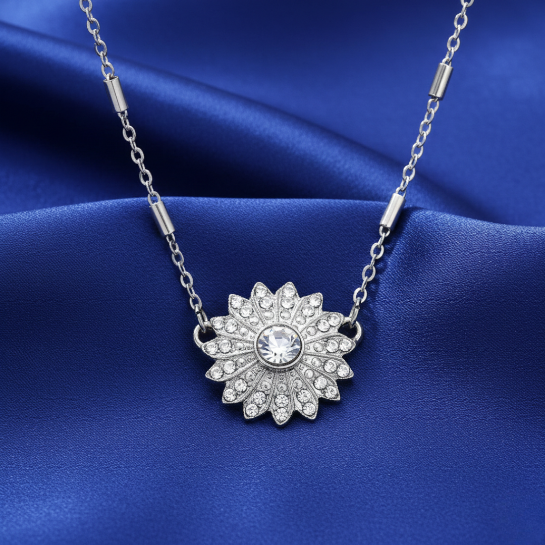Silver necklace with a floral pendant littered with crystals on a blue fabric background