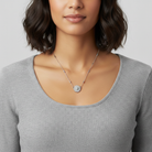 Woman wearing a silver necklace with a floral pendant full of crystals on a plain background