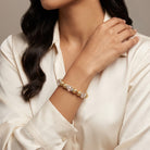 Woman wearing a gold tone and clear crystal bracelet with a white outfit