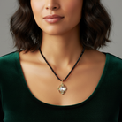 Woman wearing a black beaded necklace with a gold pendant and a large clear crystal against a neutral background