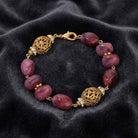 Bracelet with purple beads and gold filigree ends on a dark fabric background