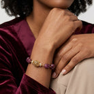 Person wearing a gold bracelet with purple beads on a blurred background