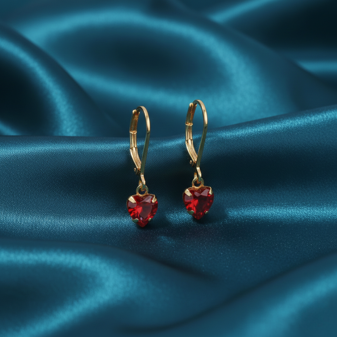 Gold earrings with red heart-shaped stones on a blue satin background