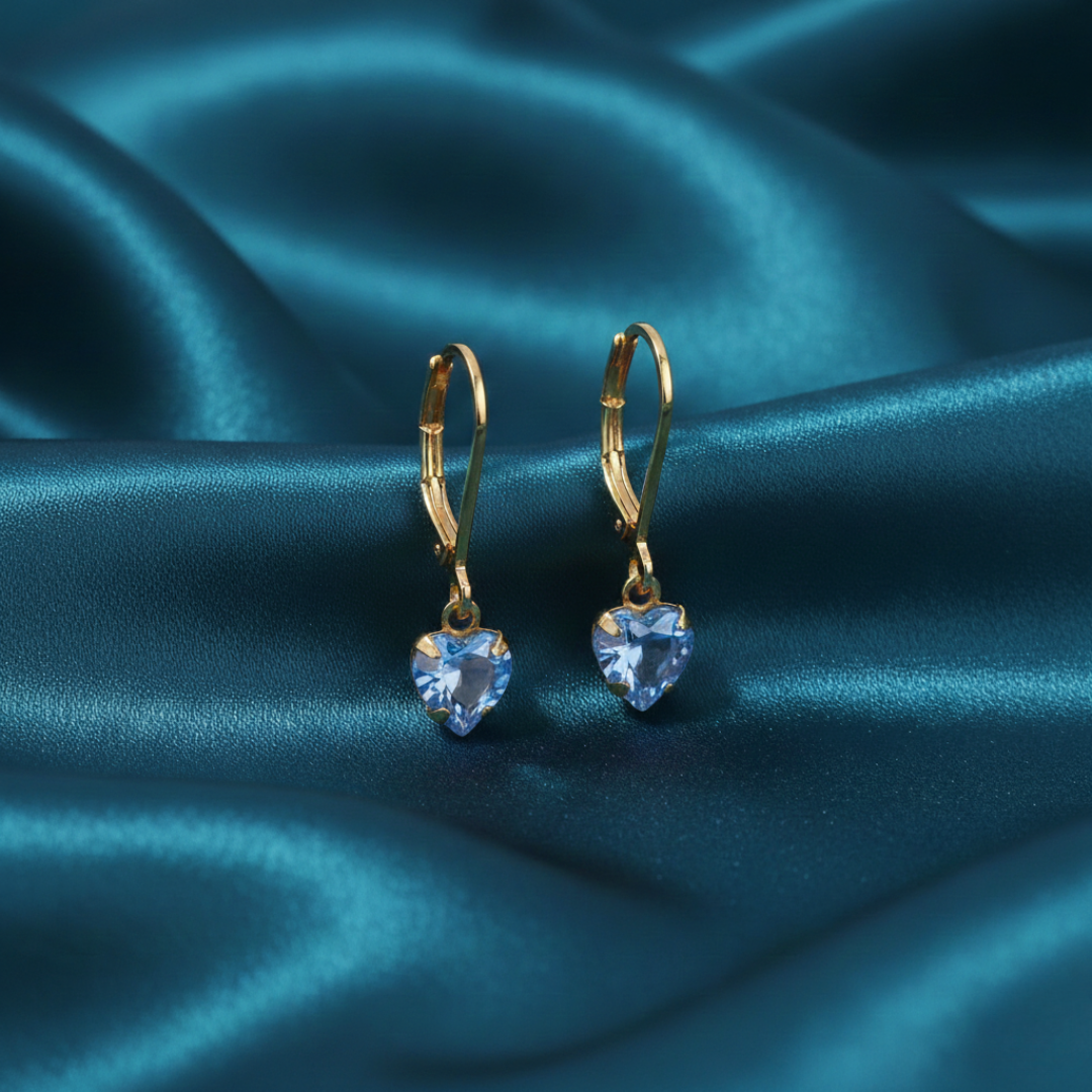 Gold earrings with heart-shaped blue gemstones on a blue satin background