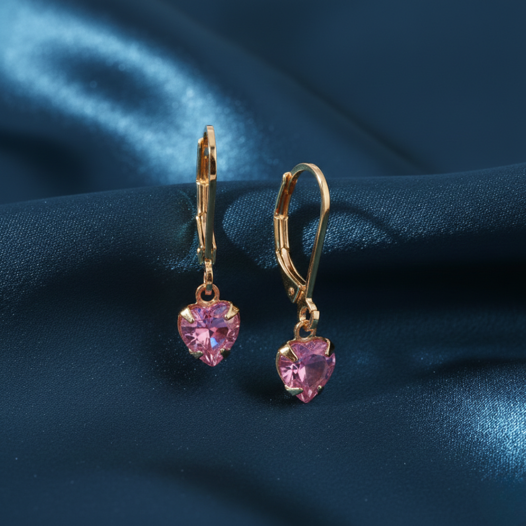 Gold heart-shaped earrings with pink gemstones on a blue fabric background
