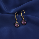 Gold heart-shaped earrings with purple crystals on a blue fabric background