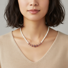 Woman wearing a pearl necklace with purple beads against a neutral background