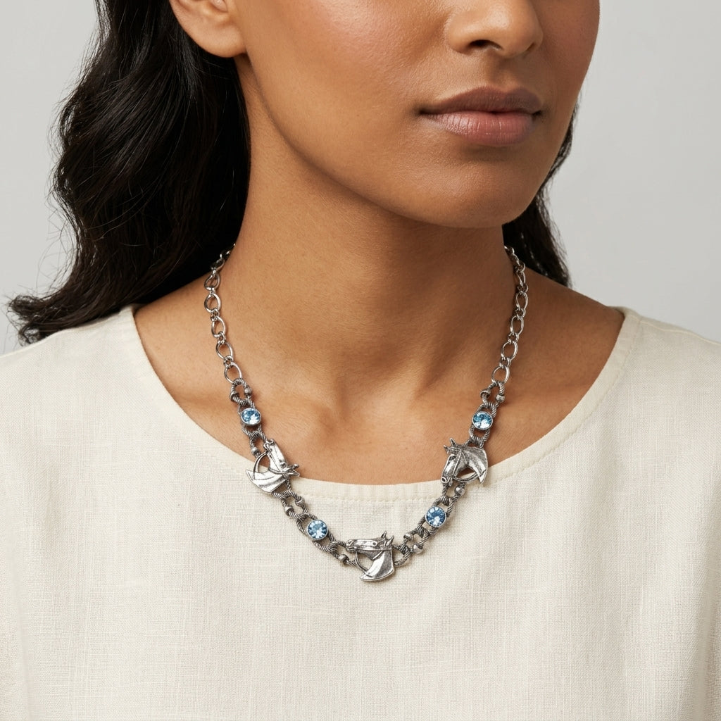 Woman wearing a silver necklace with horse charms and blue crystals on a plain background