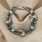 Silver bracelet with horse head designs and blue crystals on a beige fabric surface