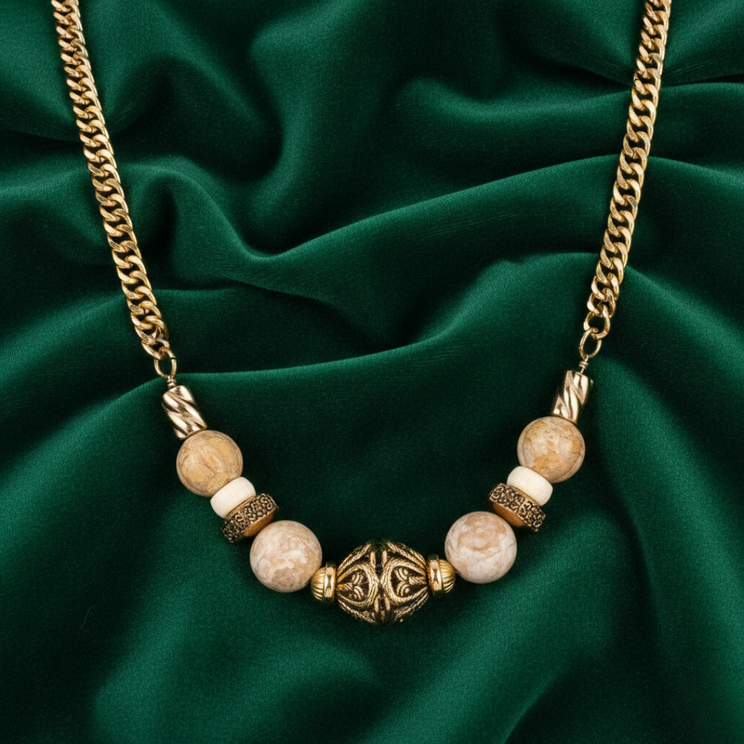 Necklace with gold chain and stone beads on a green fabric background