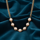 Champaign-colored faux pearl necklace with gold chain on a blue fabric background
