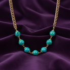 Necklace with turquoise beads and gold chain on a purple fabric background