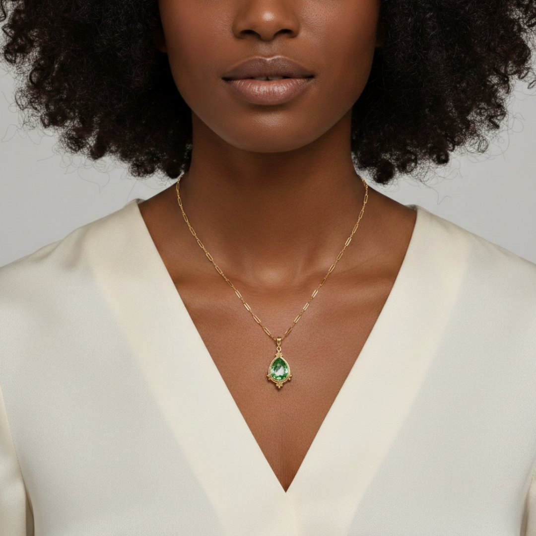 Woman wearing a gold necklace with a green pendant against a neutral background