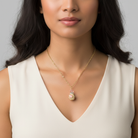 Woman wearing a gold necklace with a pendant against a neutral background