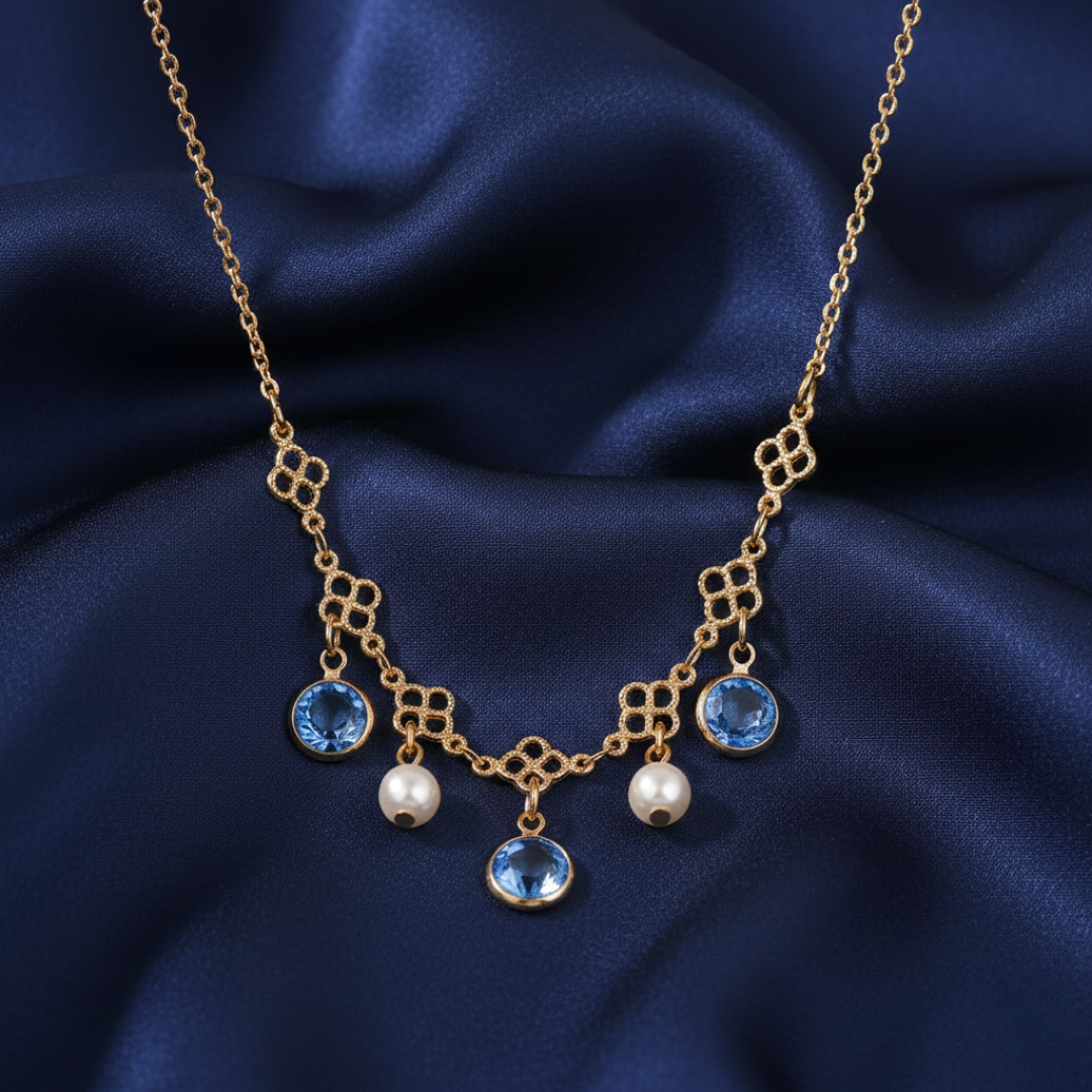 Gold necklace with blue gemstones and faux pearls on a dark blue fabric background