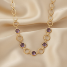 Gold necklace with purple gemstones on a beige fabric background