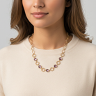 Woman wearing a gold and purple beaded necklace against a neutral background