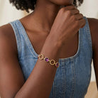 Woman wearing a gold bracelet with purple Austrian crystals on a neutral background