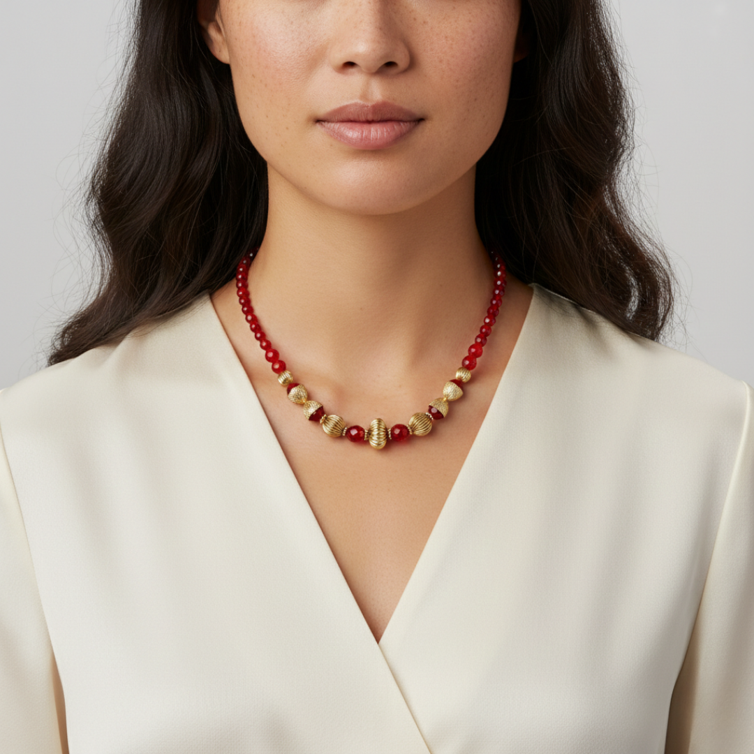 Woman wearing a red and gold beaded necklace against a plain background