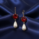 Pair of earrings with red crystals and faux pearl drops on a blue satin background