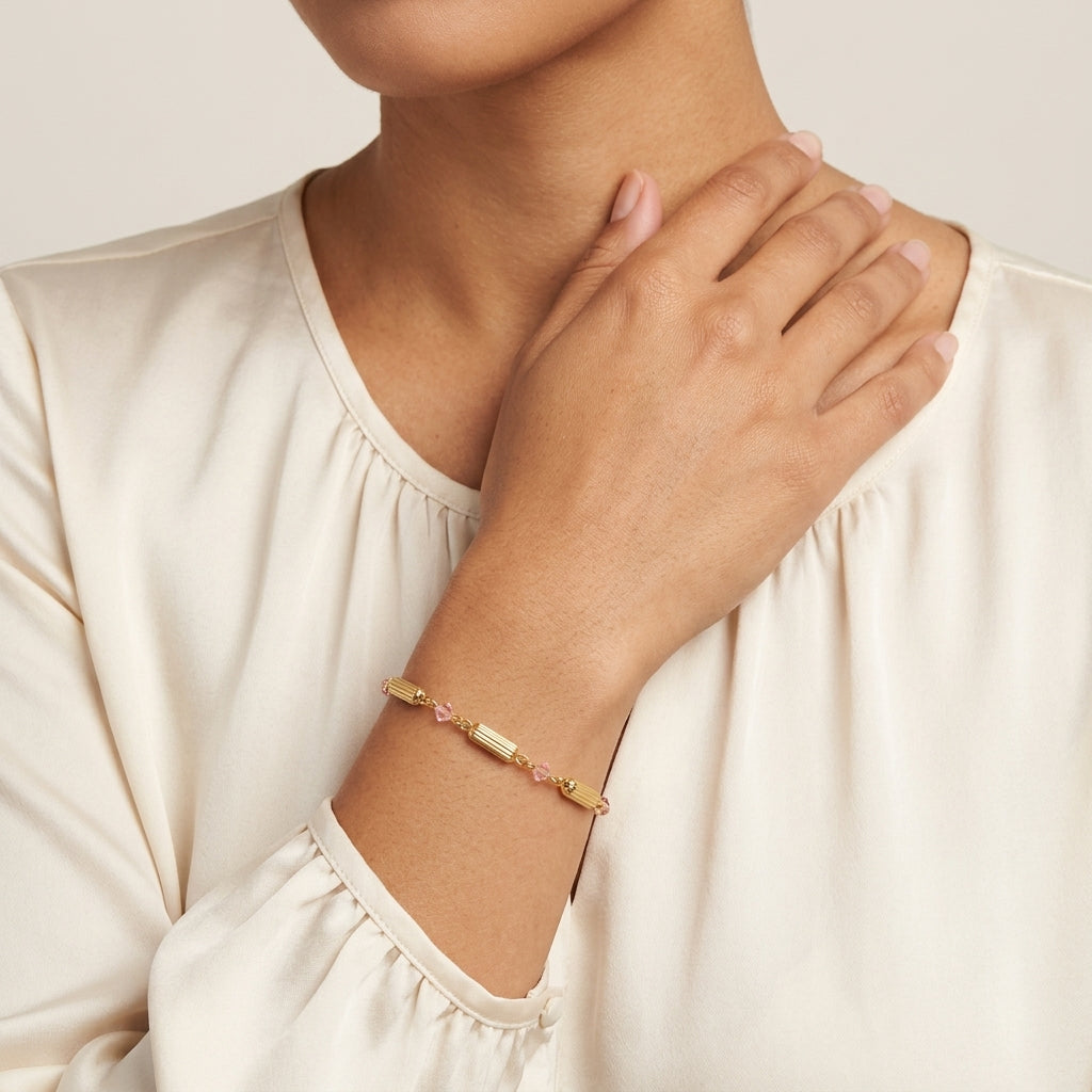 Gold bracelet with pink glass crystals on a person's wrist against a neutral background