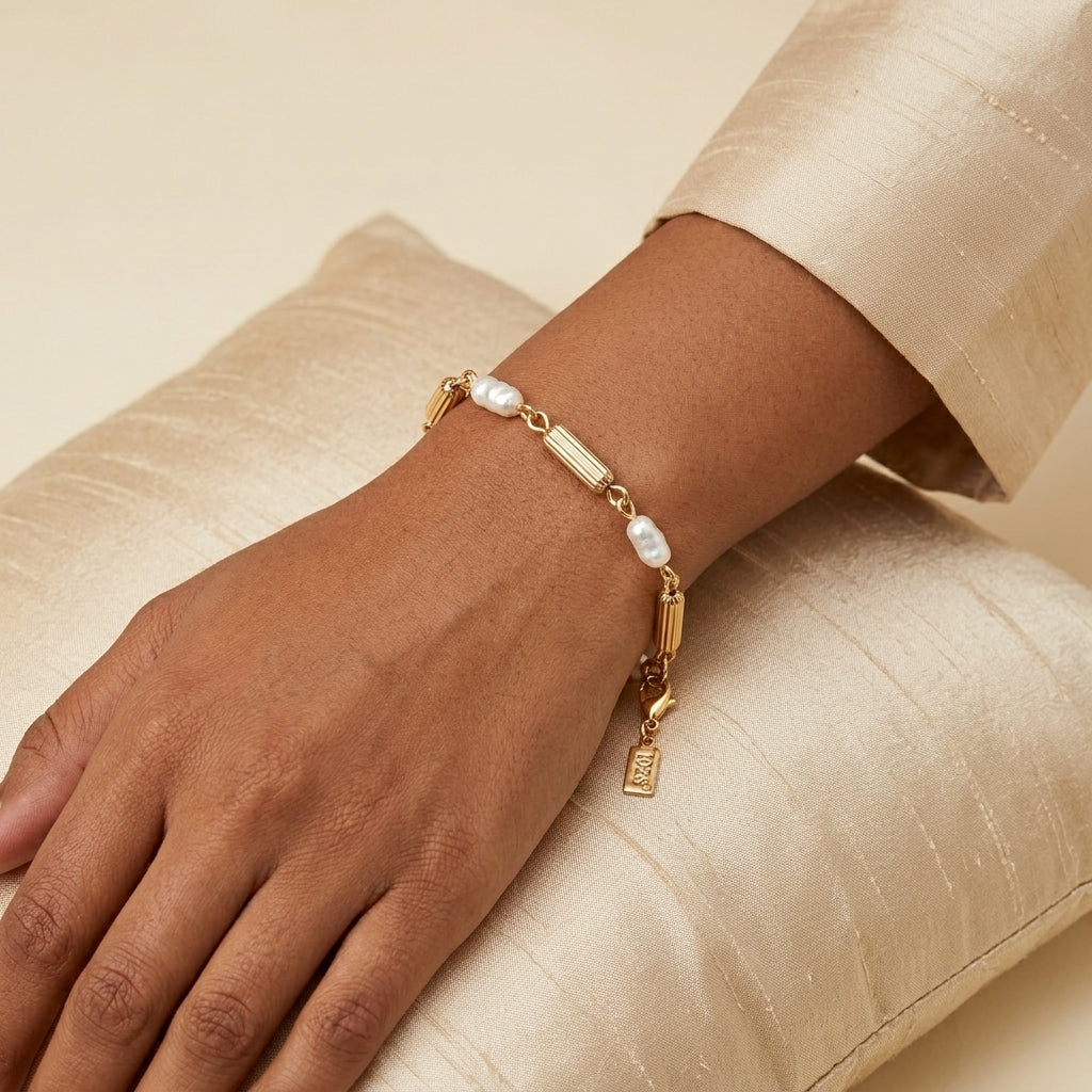 Gold bracelet with pearls on a wrist against a beige background