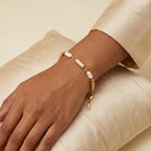 Gold bracelet with pearls on a wrist against a beige background