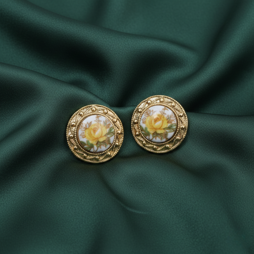 Gold earrings with floral design on a green fabric background