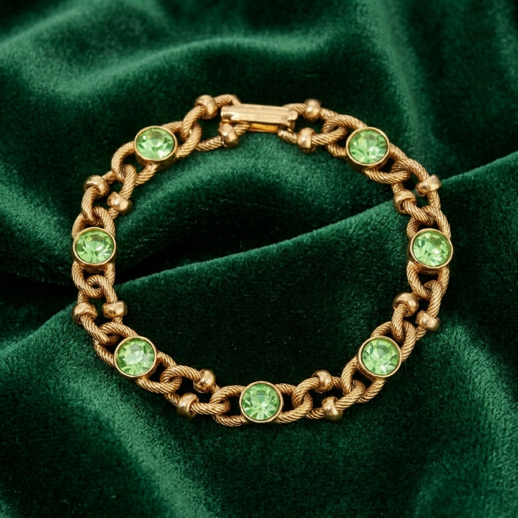 Gold tone chain bracelet with green crystals on a green fabric background