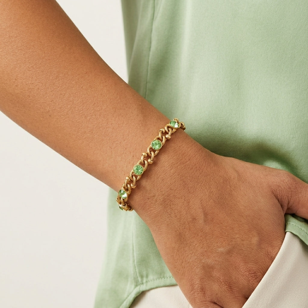 Gold bracelet with green crystals on a wrist against a light green background