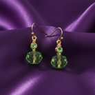 Green crystal earrings with gold accents on a purple satin background