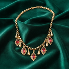Gold necklace with red gemstones on a green fabric background