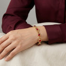 Gold bracelet with red stones on a wrist against a neutral background