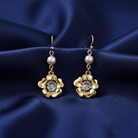 Gold floral earrings with faux pearls on a blue satin background