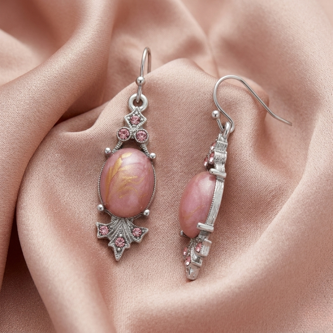 Pair of pink stone earrings with silver detailing on a soft pink fabric background