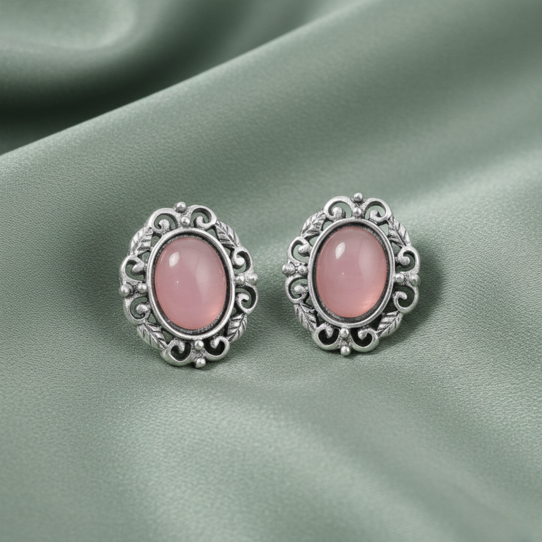 Pair of silver earrings with pink gemstones on a green fabric background