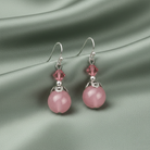 Pink crystak earrings with silver hooks on a gray fabric background