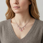 Woman wearing a delicate necklace with pink stones and crystals against a neutral background