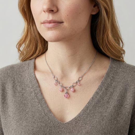 Woman wearing a delicate necklace with pink stones and crystals against a neutral background