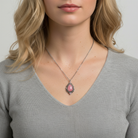 Woman wearing a necklace with a pink pendant with crystals against a neutral background