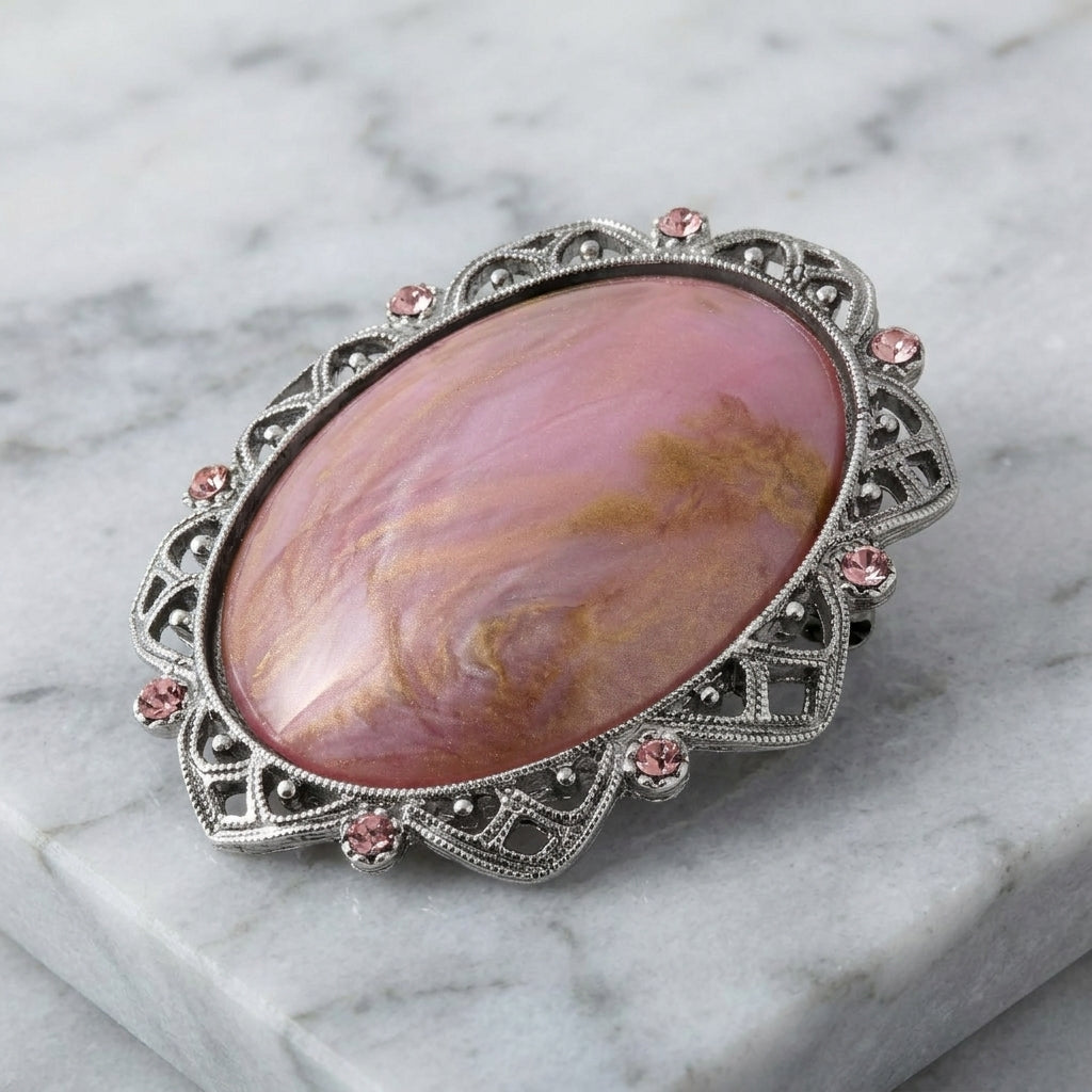 Decorative brooch with pink stone and pink crystals on a silver frame on a marble surface