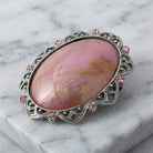 Decorative brooch with pink stone and pink crystals on a silver frame on a marble surface