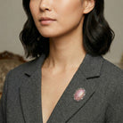 Woman wearing a gray blazer with a pink brooch against a neutral background